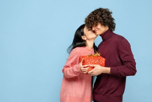 Devojka poklanja dečku poklon i ljubi ga u obraz.